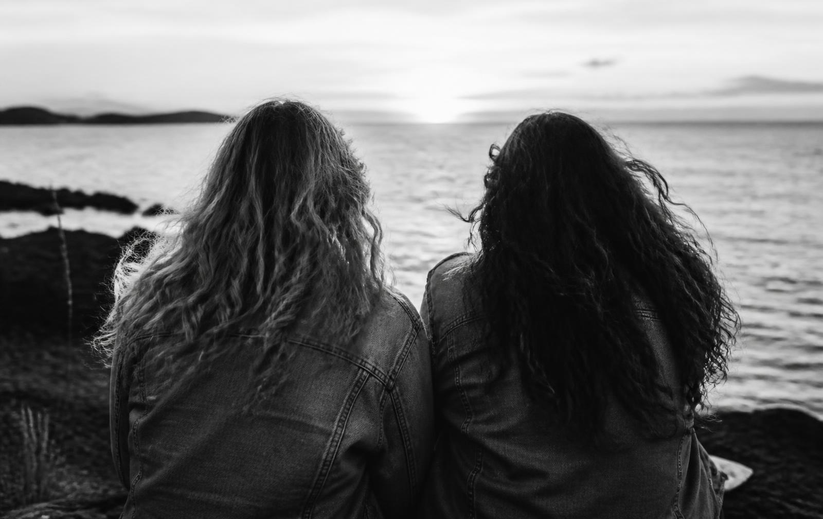 Two people sitting side by side looking out at the sea, black and white